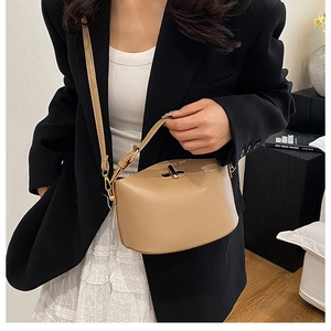 Detail view of the beige leather handbag featuring a golden twist lock and adjustable strap