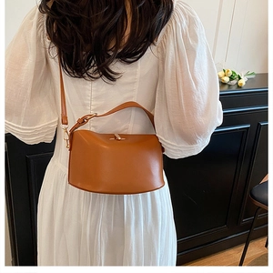 Detailed view of a brown leather shoulder bag with gold metal clasp on a model