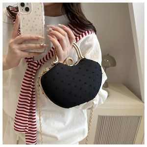 Detail of heart-shaped handbag featuring black embossed texture and gold metal handle