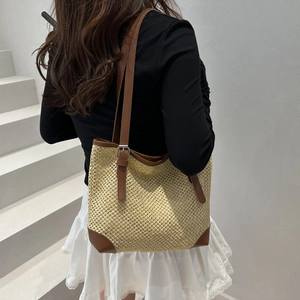 Summer woven straw tote bag with brown leather trim shown on shoulder in a lifestyle setting