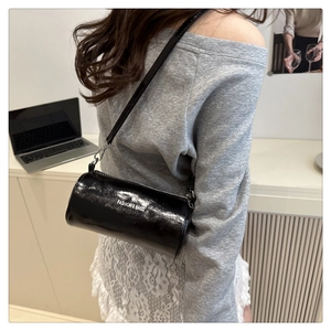 Détail d'un sac cylindrique noir avec finition brillante et lettrage Fashion & Bags