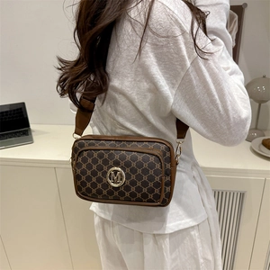 Retro brown monogram camera bag with wide strap and gold M logo in minimalist interior