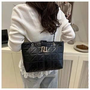 Detail of a black quilted leather tote bag with a golden metal buckle and chain strap