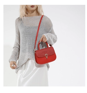 Détail du sac rouge avec rabat pailleté et boucle en U dorée porté sur un tricot gris clair
