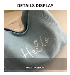 Detail of light blue denim tote with white Hello cursive embroidery and soft fabric texture