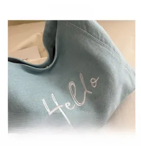 Detail of light blue denim tote with white Hello cursive embroidery and soft fabric texture