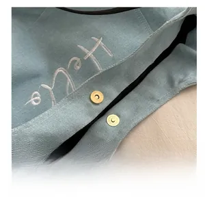 Detail of light blue denim tote with magnetic gold clasp and white letter embroidery