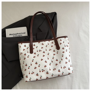 Close-up of stylish cherry print tote bag with brown handles on soft fabric backdrop