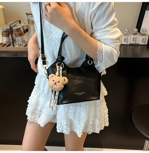 Detail of black leather handbag with golden lettering and cute brown plush bear charm
