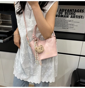 Pink bucket handbag with knotted handle, plush bear charm, and removable shoulder strap