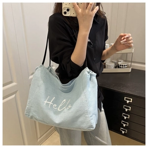 Detail of light blue denim tote bag featuring white Hello embroidery and black straps