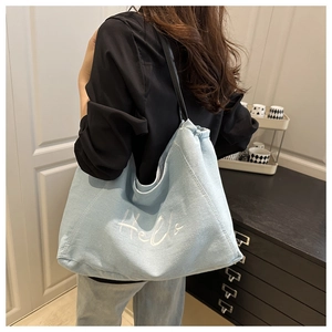 Détail du sac cabas en denim bleu clair avec broderie Hello blanche sur un mannequin