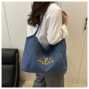 Detail of large navy denim tote bag with yellow Hello embroidery and black straps