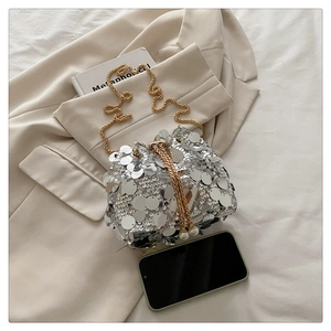 Detail view of silver sequin bucket bag with gold chain strap and smartphone for size scale