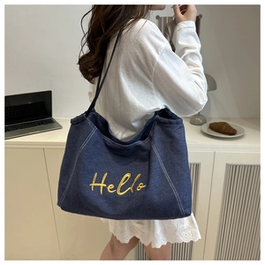 Detail of blue denim tote bag with Hello embroidery worn by model in a cafe setting