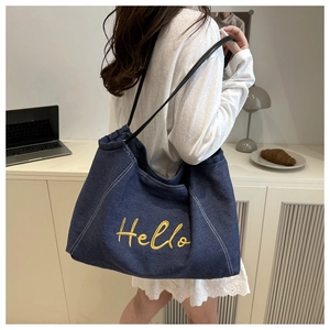 Close-up of denim tote bag featuring yellow Hello embroidery and black leather strap