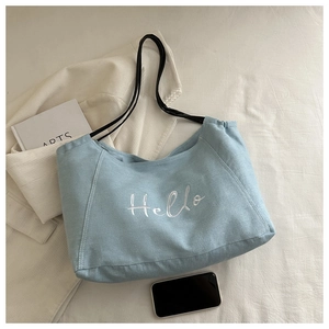 Détail du sac cabas en toile bleu clair avec broderie Hello et fines anses noires