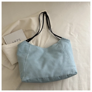 Close-up of light blue denim tote bag with black leather straps on white bedding