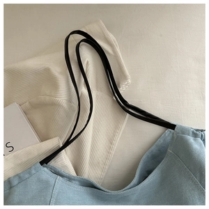 Détail de la texture en denim bleu clair et anses en cuir noir du sac à bandoulière