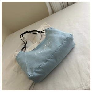 Détail d'un cabas en denim bleu clair avec broderie Hello blanche et anses noires fines