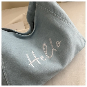 Gros plan d'un cabas en jean bleu clair avec broderie Hello blanche et texture du tissu