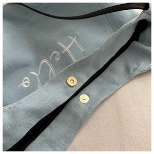 Gros plan du sac en denim bleu clair avec broderie Hello blanche et fermoir magnétique