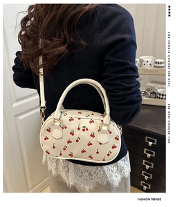 Detail shot of a white cherry print crossbody bag with detachable strap and golden hardware