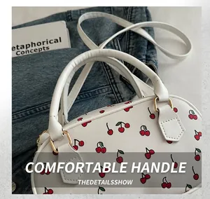 Detailed view of the red cherry print on white leather cylinder bag with golden hardware