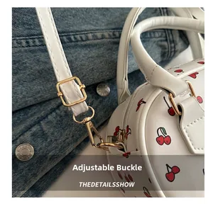 Detailed macro of gold metal adjustment buckle and cherry print on white crossbody bag