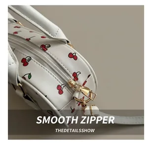 Detailed close-up of golden metal zipper and cherry print on white leather bag