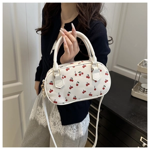 Detailed view of a white cherry print barrel bag held by a model for a chic summer look