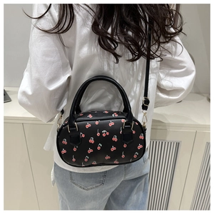 Back view of a black cherry print crossbody bag worn by a model in a white shirt