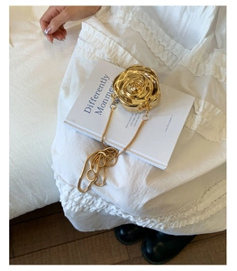 Detail of a 3D gold rose clutch bag with a metallic finish and a sleek snake chain strap