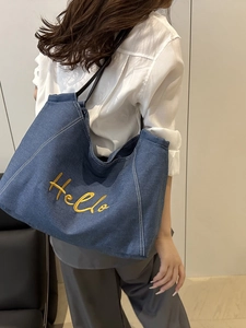 Sac fourre-tout en denim bleu avec broderie Hello jaune et anses en cuir noir sur mannequin