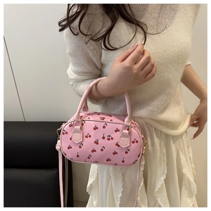 Pink Boston bag with cherry prints and gold hardware shown on a model in a white outfit