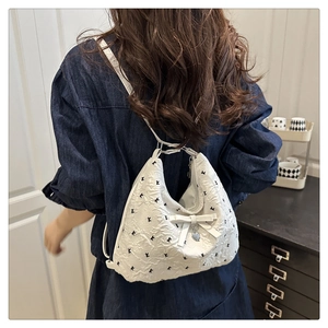 Détail du sac hobo blanc avec broderie noire, nœud et pendentif en forme de cœur