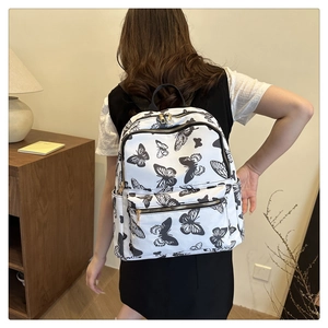 Detail of white nylon backpack featuring black butterfly print and gold zippers on model