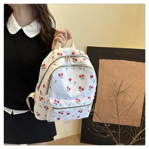 Detailed view of white nylon backpack featuring cherry prints and gold zipper hardware