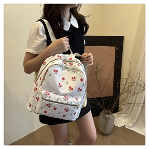 Detail view of the white canvas backpack featuring vibrant red cherry and leaf patterns