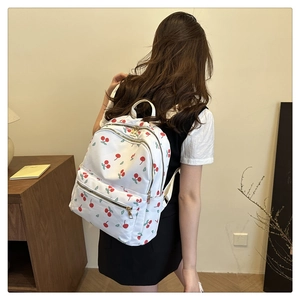 Close-up of white nylon backpack with cherry pattern and gold zippers on a model