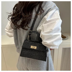 Detail of elegant black shimmering handbag with gold twist lock on a minimalist model