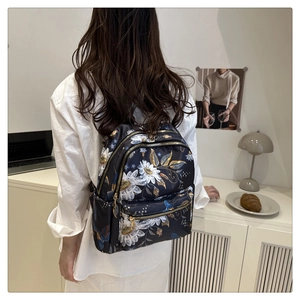 Rear view of a stylish black floral backpack with gold patterns and functional zip pockets