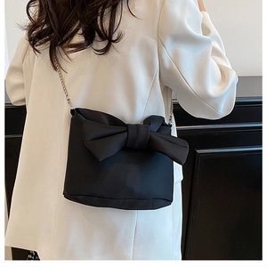 Detailed view of black bucket bag featuring a large bow and elegant metal chain strap