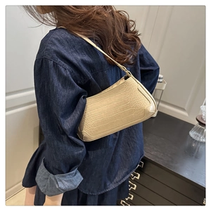 Detail of cream baguette bag with crocodile pattern texture worn by model in denim