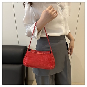 Detail of red crocodile pattern baguette bag worn by model with white shirt and gray pants