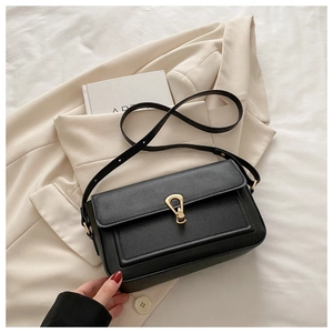 Gros plan d'un sac bandoulière en cuir noir avec boucle dorée sur un tissu blanc doux