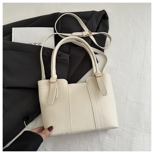 Detail of cream white pebbled leather bucket bag with gold hardware on a black blazer