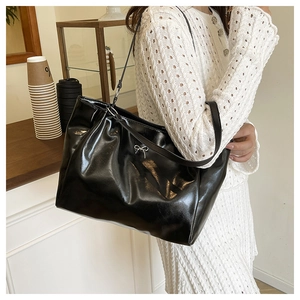 Detail of glossy black tote bag with silver bow accent worn with white dress
