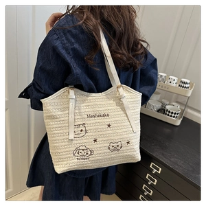 Detail of white woven tote bag with cat embroidery and leather straps on shoulder