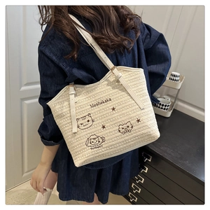 Detail of woven straw tote bag featuring cute cat embroidery and adjustable strap